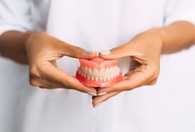 Hands holding full set of dentures at abdomen level