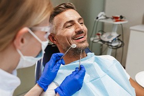 Man smiling as dentist approaches with mirror to examine his mouth
