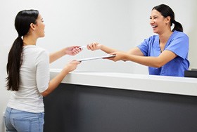 Smiling dental assistant handing patient form
