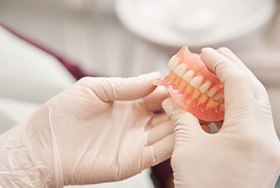 White-gloved hands holding complete set of shiny dentures