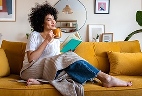 Woman relaxing on couch while reading and drinking tea
