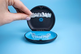 Fingers placing Invisalign tray into its carrier case with light blue background