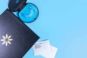 Bird’s eye view of Invisalign in its carrier case next to black folder and packages of cleaning crystals