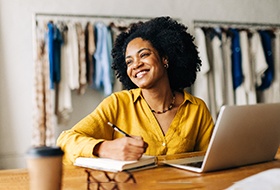 Woman in yellow shirt smiling while taking notes at work