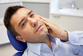 Man in dental chair holding cheek