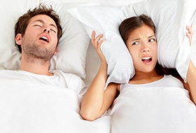 Frustrated woman covering ears next to snoring man