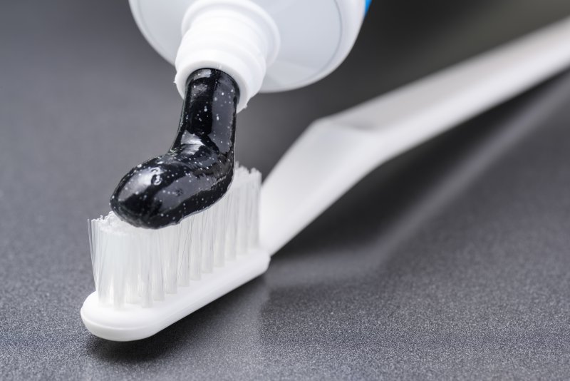 A tube of charcoal toothpaste being applied to a toothbrush.