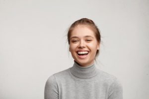 woman in gray sweater smiling after seeing cosmetic dentist