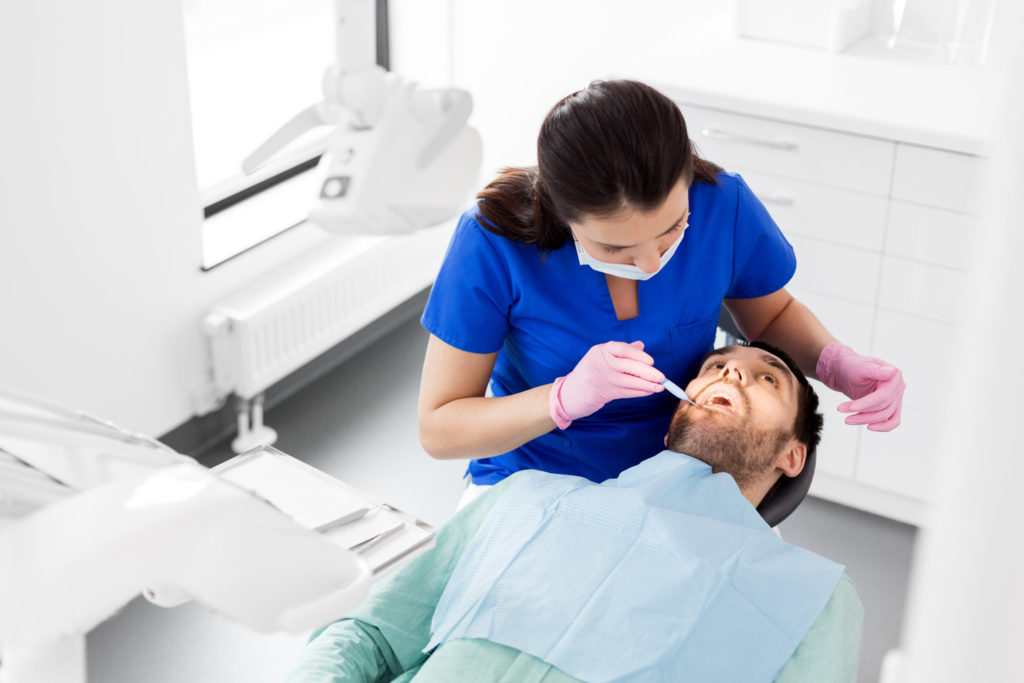 A dentist examines a patient’s mouth for signs of disease.