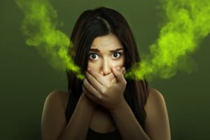 Woman covering her mouth with her hands and green odors coming from her hands