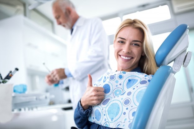 Woman at the dentist’s office smiling and giving a thumb’s up.