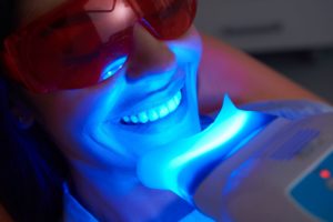 Facial view of a woman at the dentist wearing protective goggles with blue LED light shining on her teeth