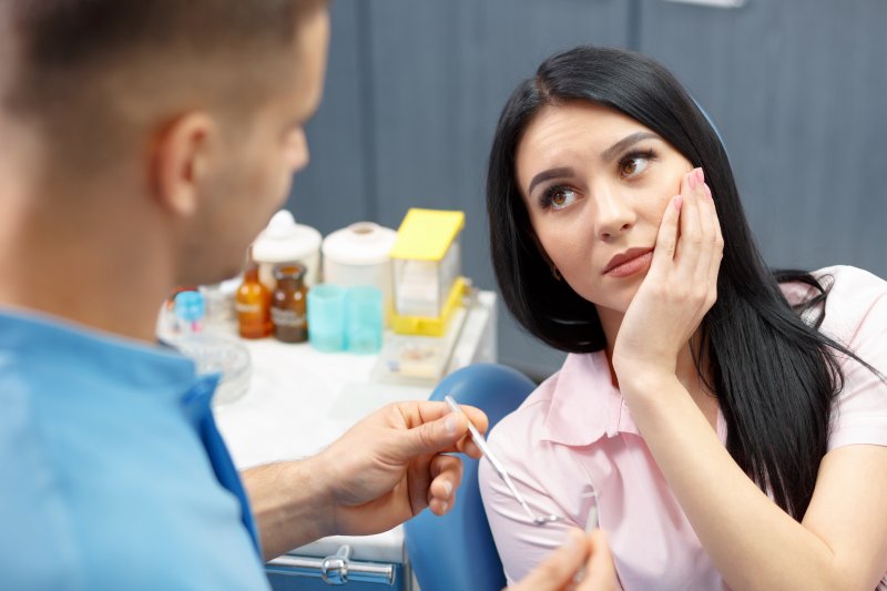 A woman holding her jaw in pain at her emergency dentist