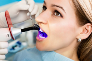 Woman sitting still as her dentist begins a teeth whitening treatment