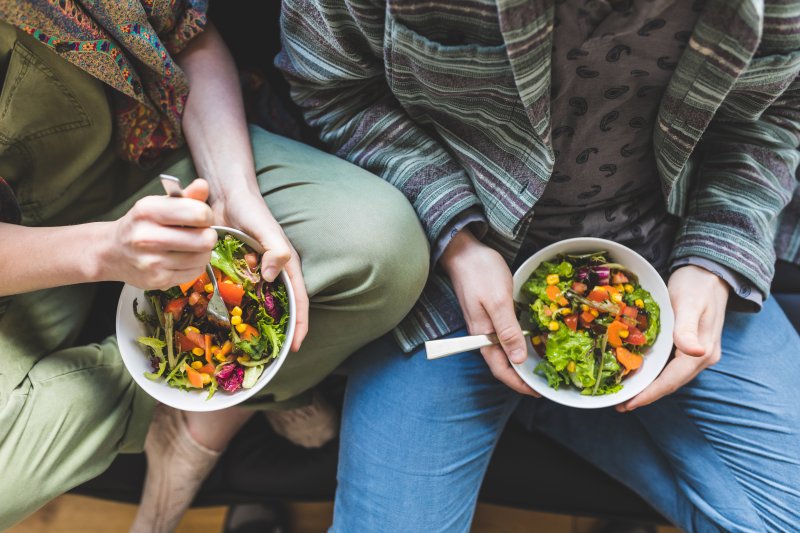 An overhead view of a couple eating healthy salads while sitting on a couch