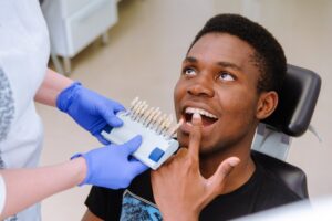 Dentist holding veneers while patient points to teeth sitting in dentist's chair.